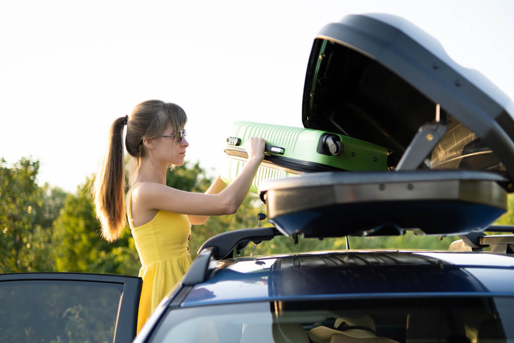 the girl takes out a green suitcase from the upper trunk of the car