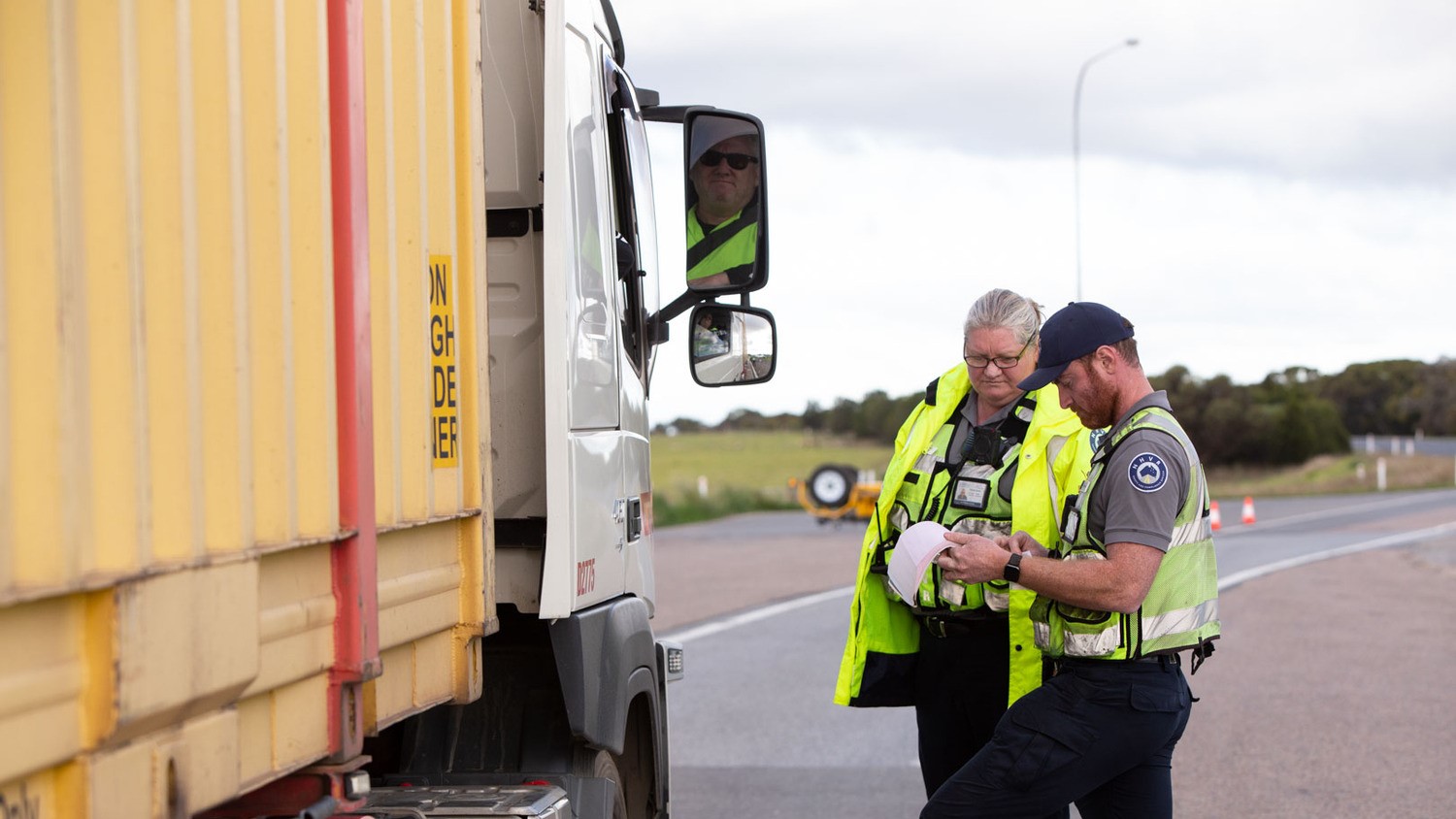 Two National Heavy Vehicle Regulator compliance officers holding paperwork check a large truck.